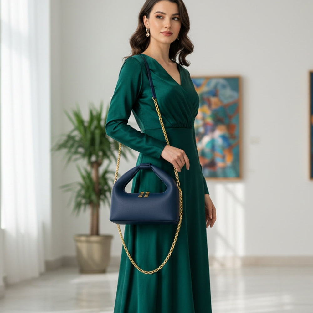 Woman in a green dress holding a blue handbag with gold chain strap in an indoor setting.