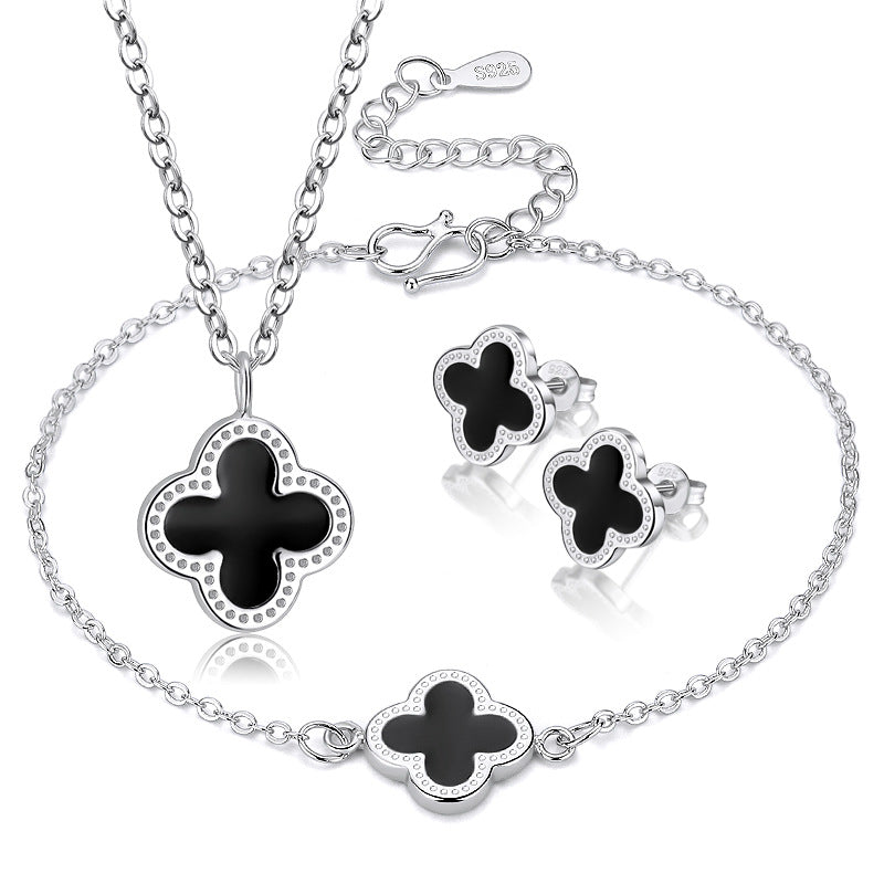 Silver jewelry set with black clover-shaped pendants on a white background