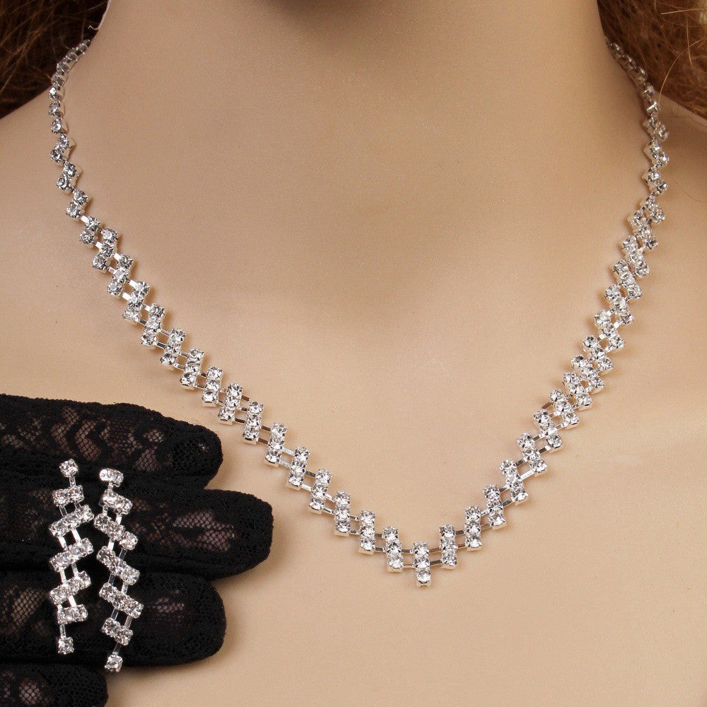 Silver necklace with clear stones on a mannequin neck, held by a black-gloved hand.