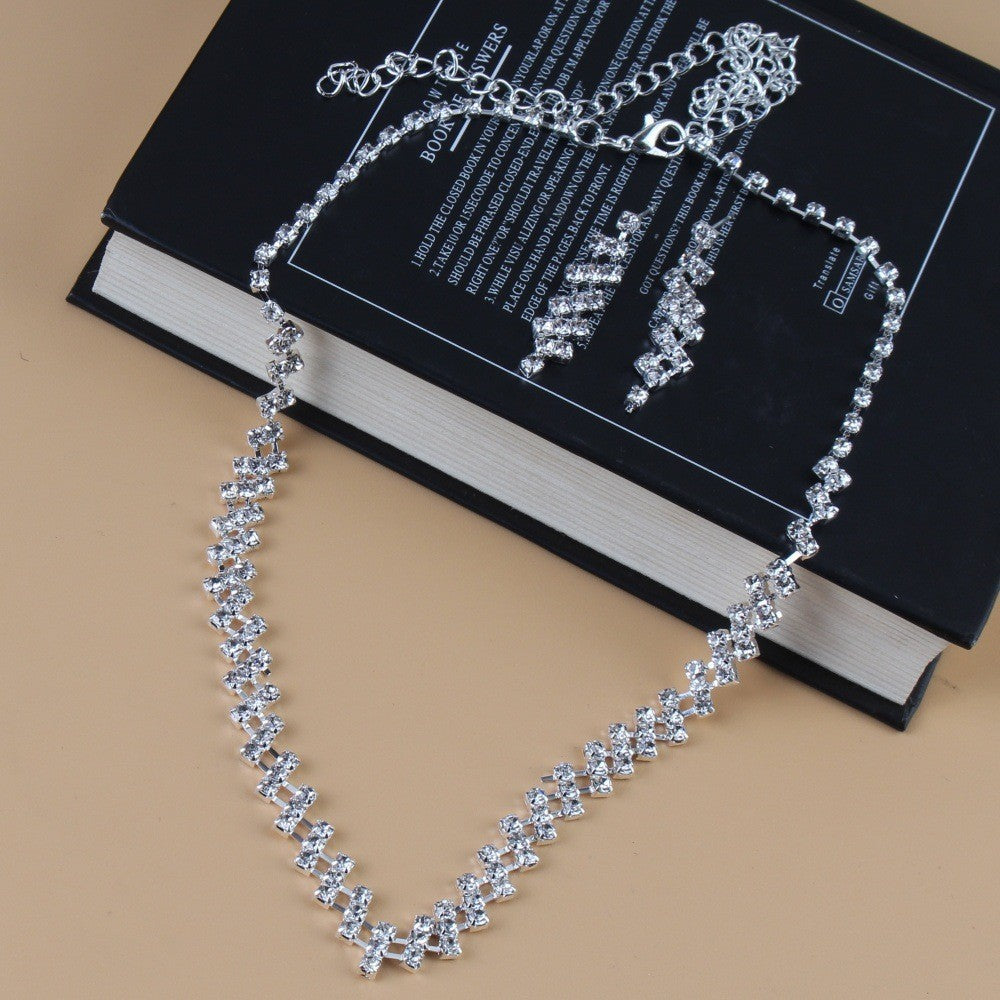 Silver necklace and earrings on a black book with a beige background