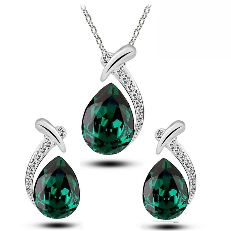 Jewelry set with green teardrop-shaped gemstones and silver chains on a white background