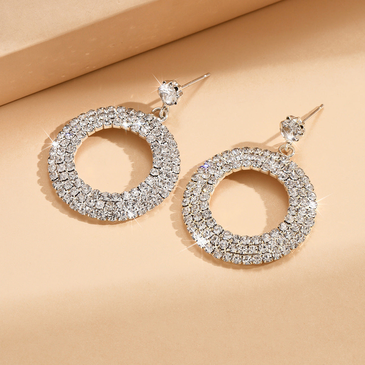 Pair of silver hoop earrings with clear gemstones on a beige background